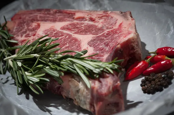 Raw dry-aged ribeye on paper with rosemary, chilli and peppercorns